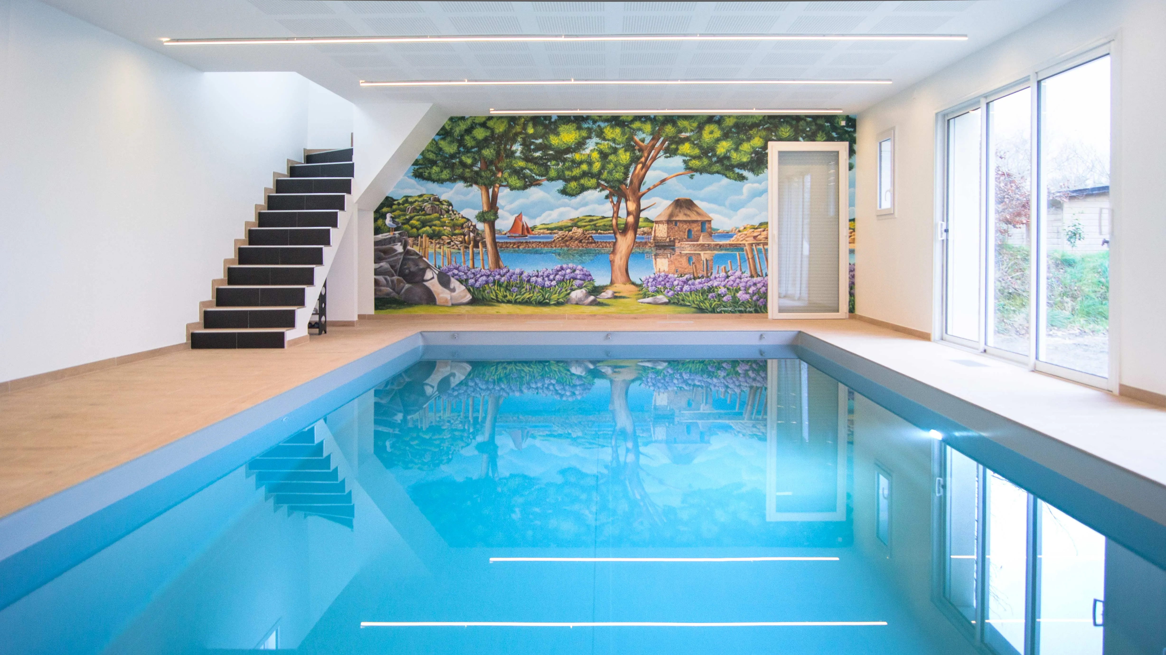 Vue de face de la fresque d'une piscine intérieure à Paimpol : moulin à marée du Birlot, agapanthes et voilier rouge sur l'archipel de Bréhat